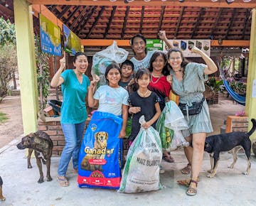 A group of volunteers and local community members in San José Manialtepec, Mexico smile and cheer while holding bags of rubbish from a river clean up.