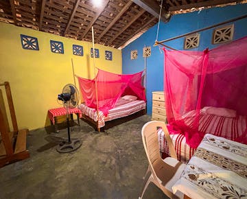 A cozy volunteer accommodation room with two beds covered by red mosquito nets.