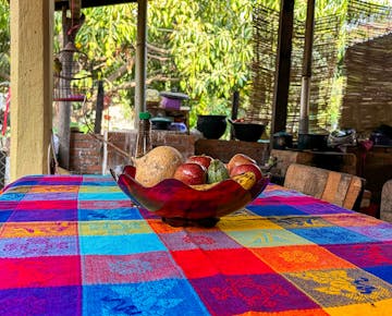 The outdoor dining table is covered with a colorful woven tablecloth featuring a bowl of fresh fruit and vegetables.