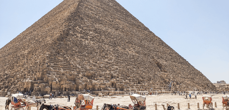 Horse-drawn carriages await visitors in front of the towering Great Pyramid of Giza under a clear blue sky, showcasing one of Egypt’s most iconic and historic landmarks.